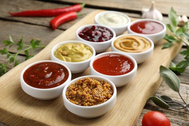 Different tasty sauces in bowls and ingredients on wooden table, closeup