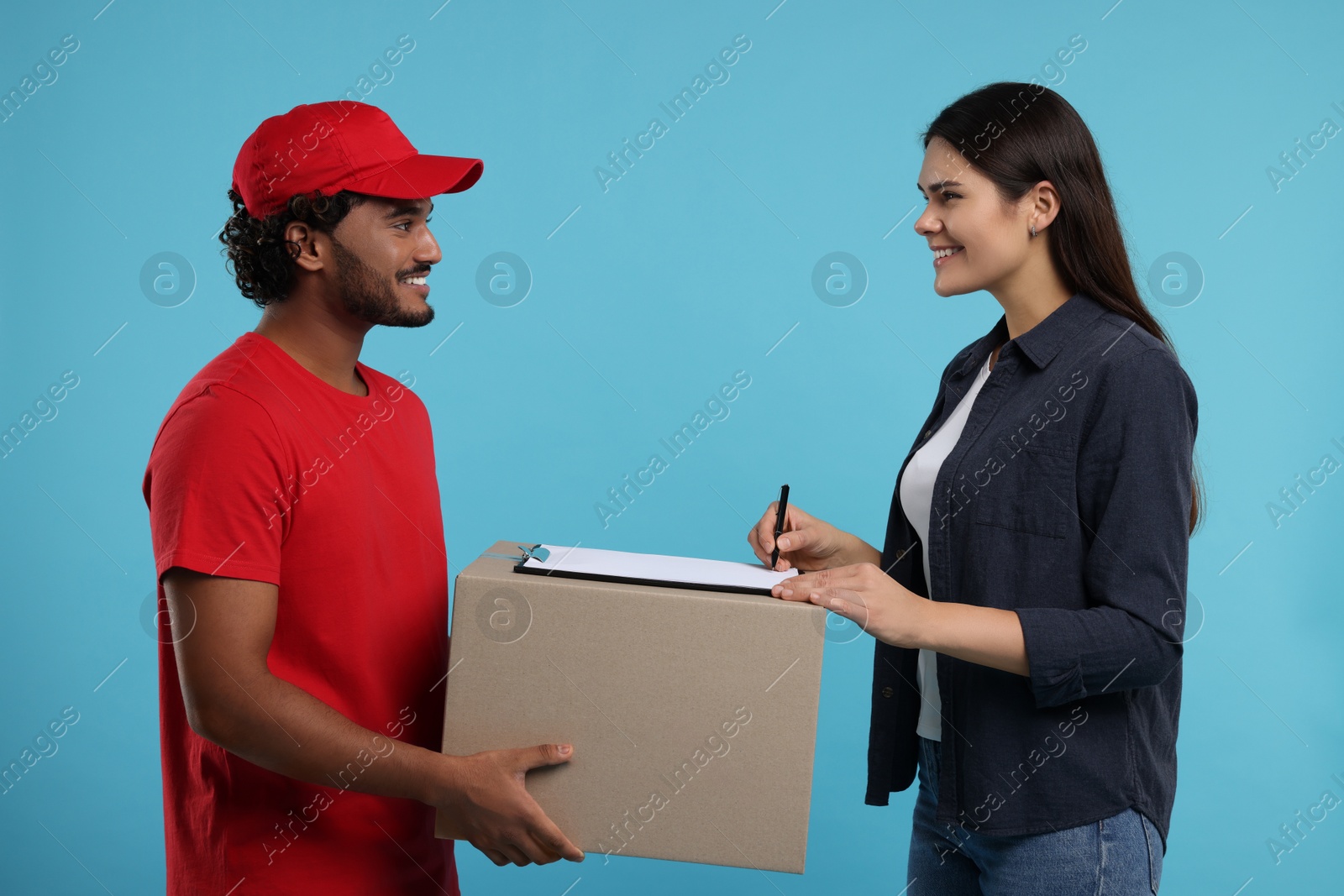 Photo of Smiling woman signing order receipt on light blue background. Courier delivery