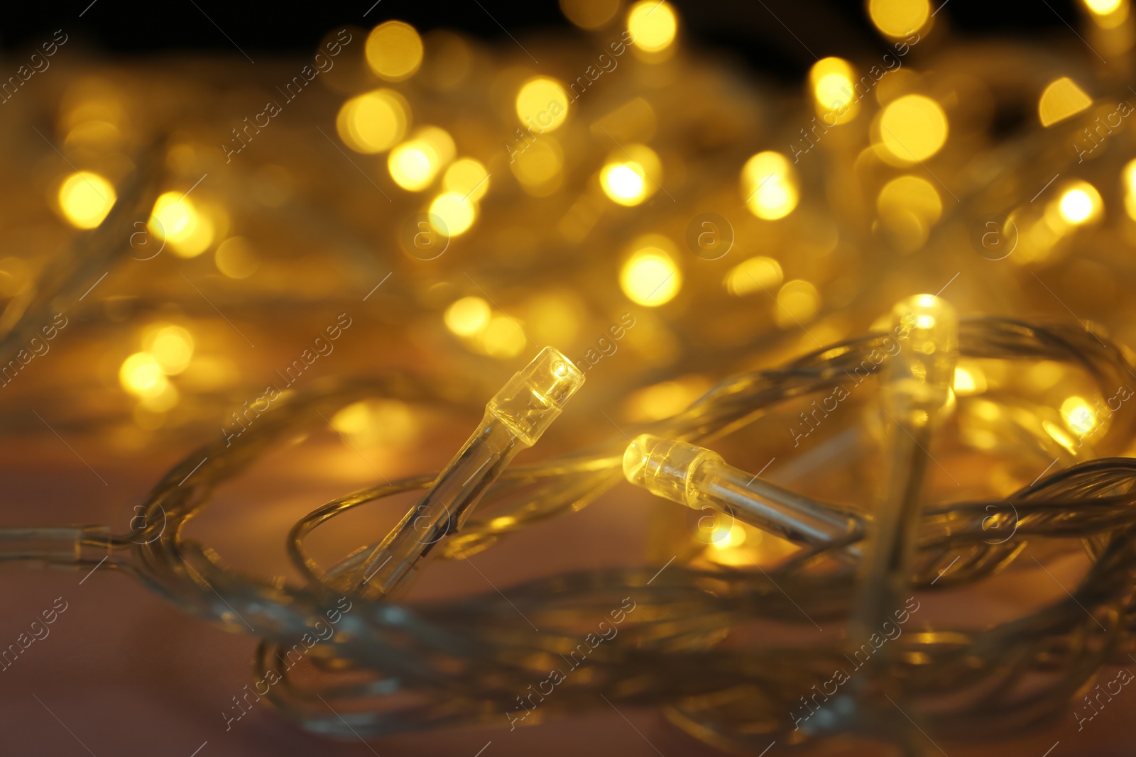 Photo of Glowing Christmas lights on color background, closeup view