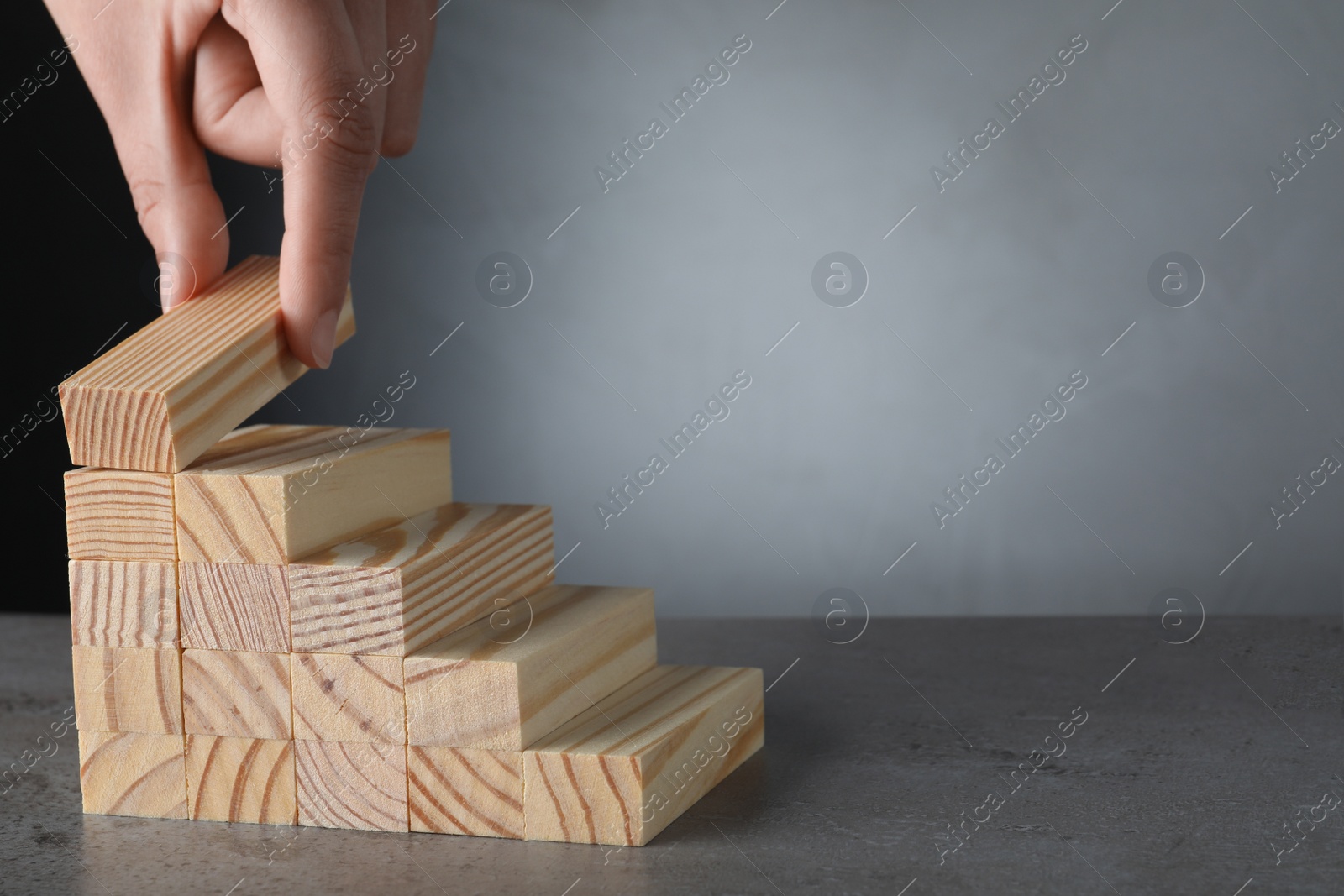 Photo of Closeup view of woman building steps with wooden blocks on grey table, space for text. Career ladder