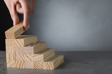 Closeup view of woman building steps with wooden blocks on grey table, space for text. Career ladder