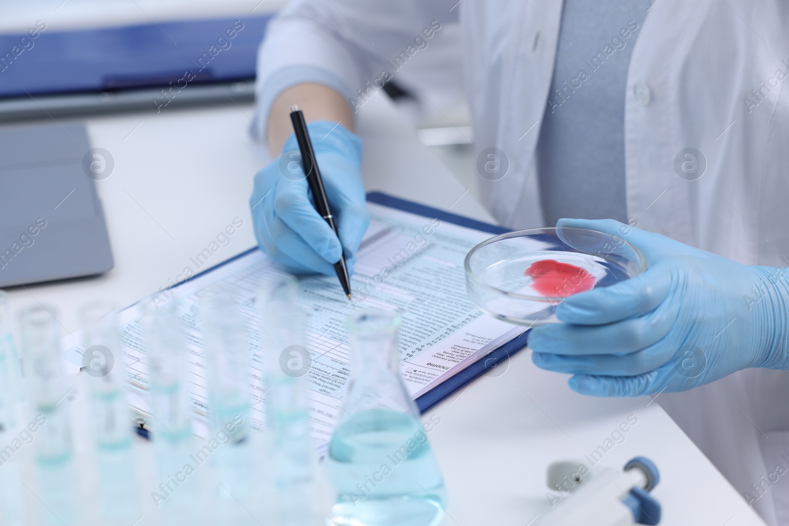 Photo of Laboratory worker holding petri dish with blood sample while working at white table, closeup