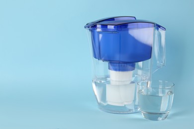 Photo of Filter jug and glass with purified water on light blue background. Space for text