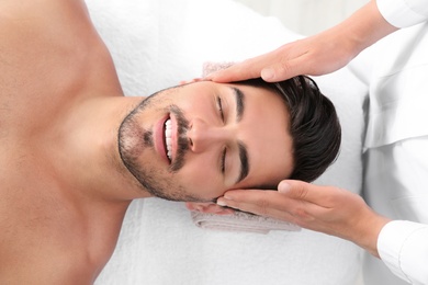 Handsome young man receiving face massage on spa table, top view