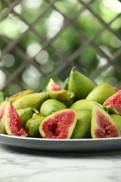 Cut and whole green figs on white marble table against blurred background, space for text