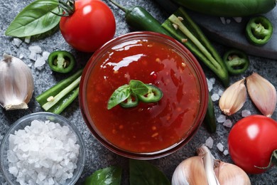 Photo of Spicy chili sauce and ingredients on grey table, flat lay