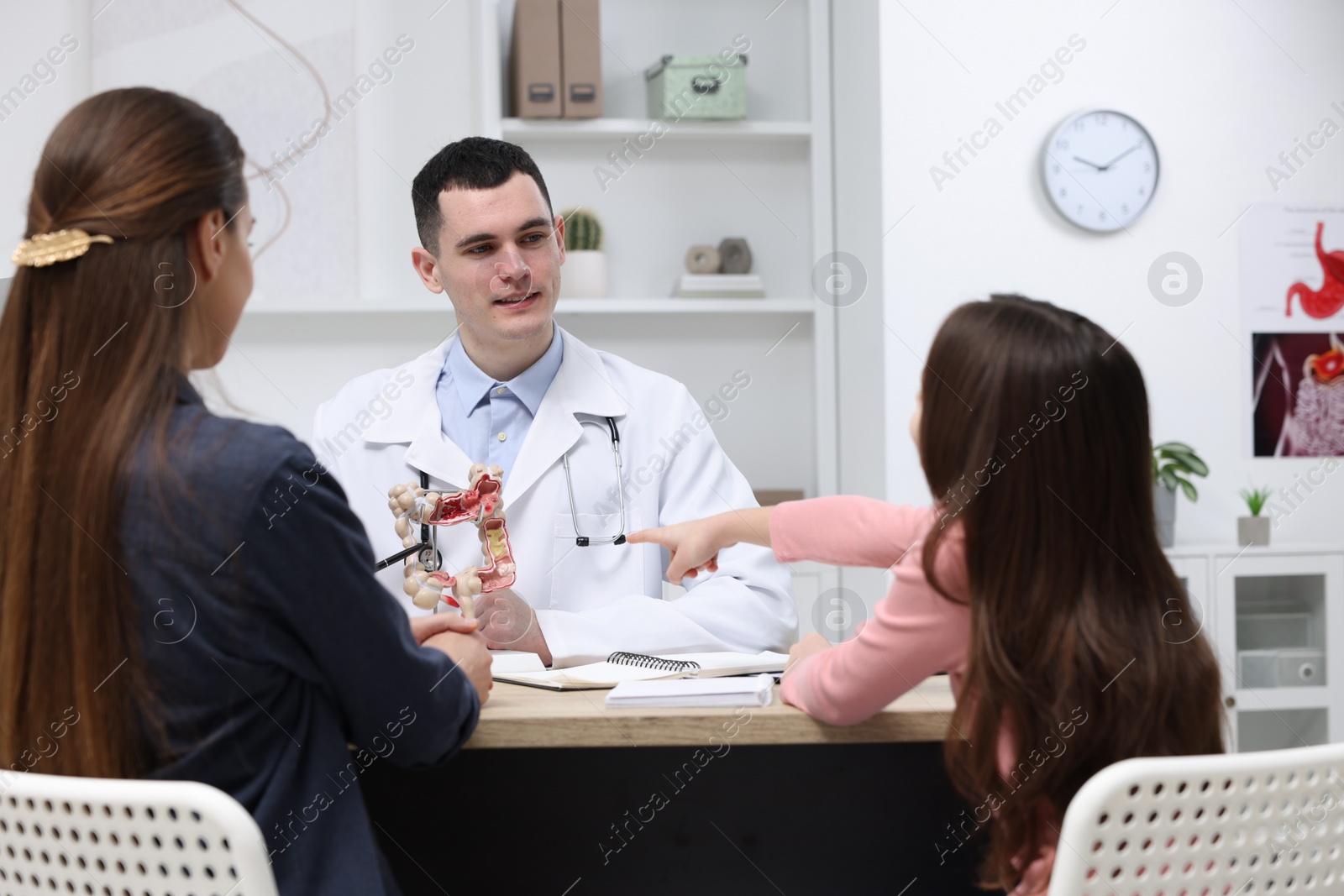 Photo of Gastroenterologist with model of intestine consulting woman and her daughter in clinic