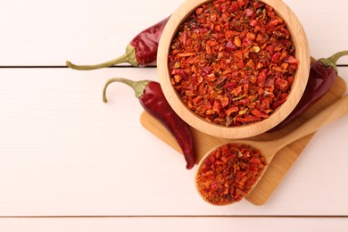 Photo of Chili pepper flakes and pods on white wooden table, flat lay. Space for text