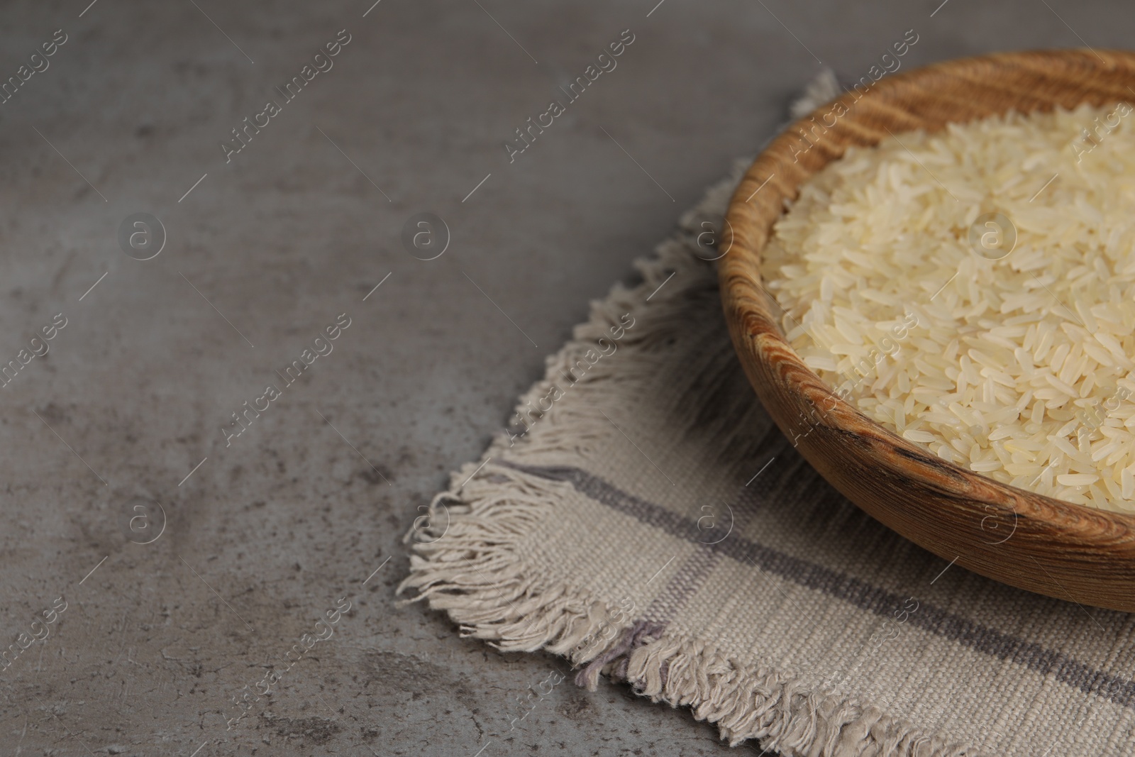Photo of Bowl of raw rice on grey table. Space for text