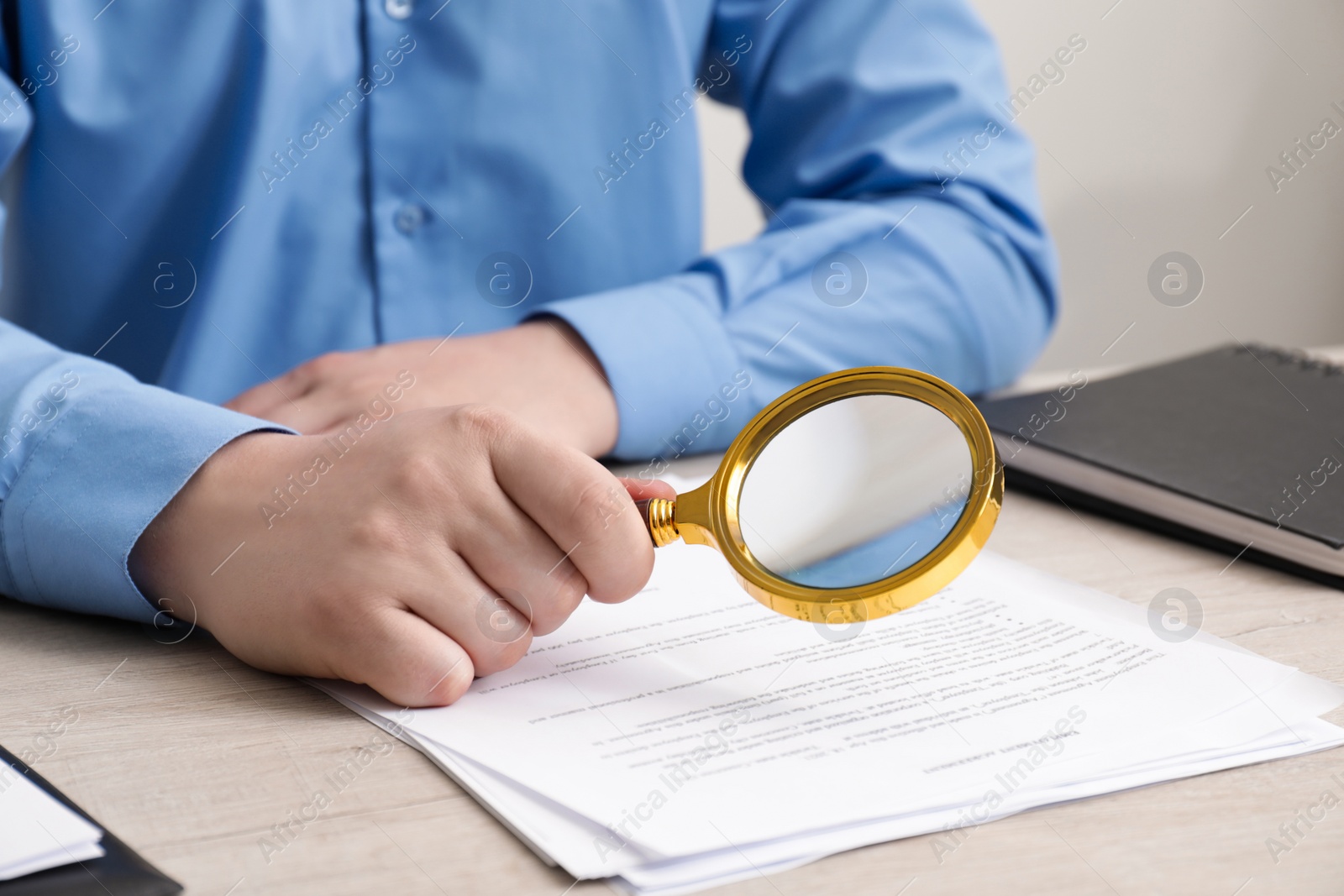 Photo of Man looking at document through magnifier at white wooden table, closeup. Searching concept