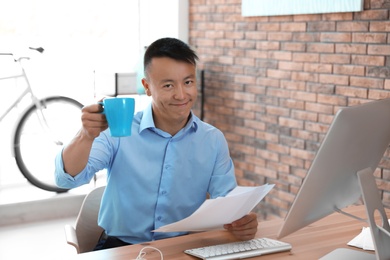 Photo of Happy young businessman with cup of coffee enjoying peaceful moment at workplace