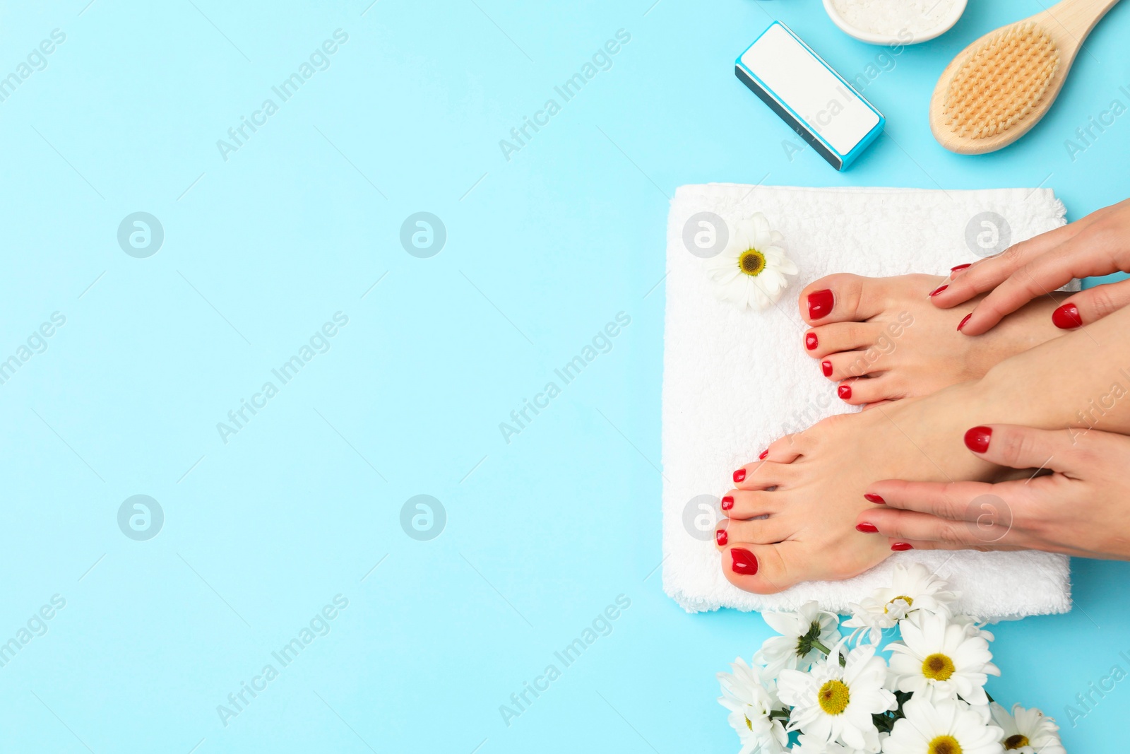 Photo of Woman with stylish red toenails after pedicure procedure and chamomile flowers on light blue background, top view. Space for text