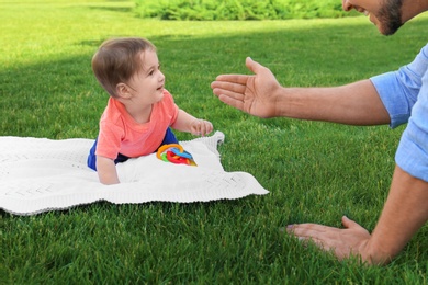 Adorable little baby crawling towards father on blanket outdoors