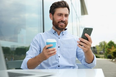 Handsome man with cup of coffee using smartphone in outdoor cafe