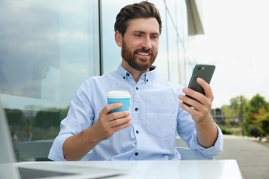 Photo of Handsome man with cup of coffee using smartphone in outdoor cafe