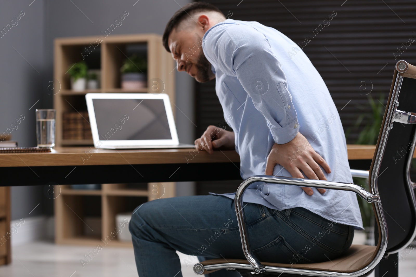 Photo of Man suffering from back pain while working with laptop in office. Symptom of poor posture