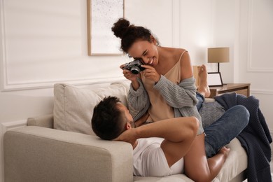 Photo of Beautiful African-American woman taking picture of her boyfriend on sofa at home