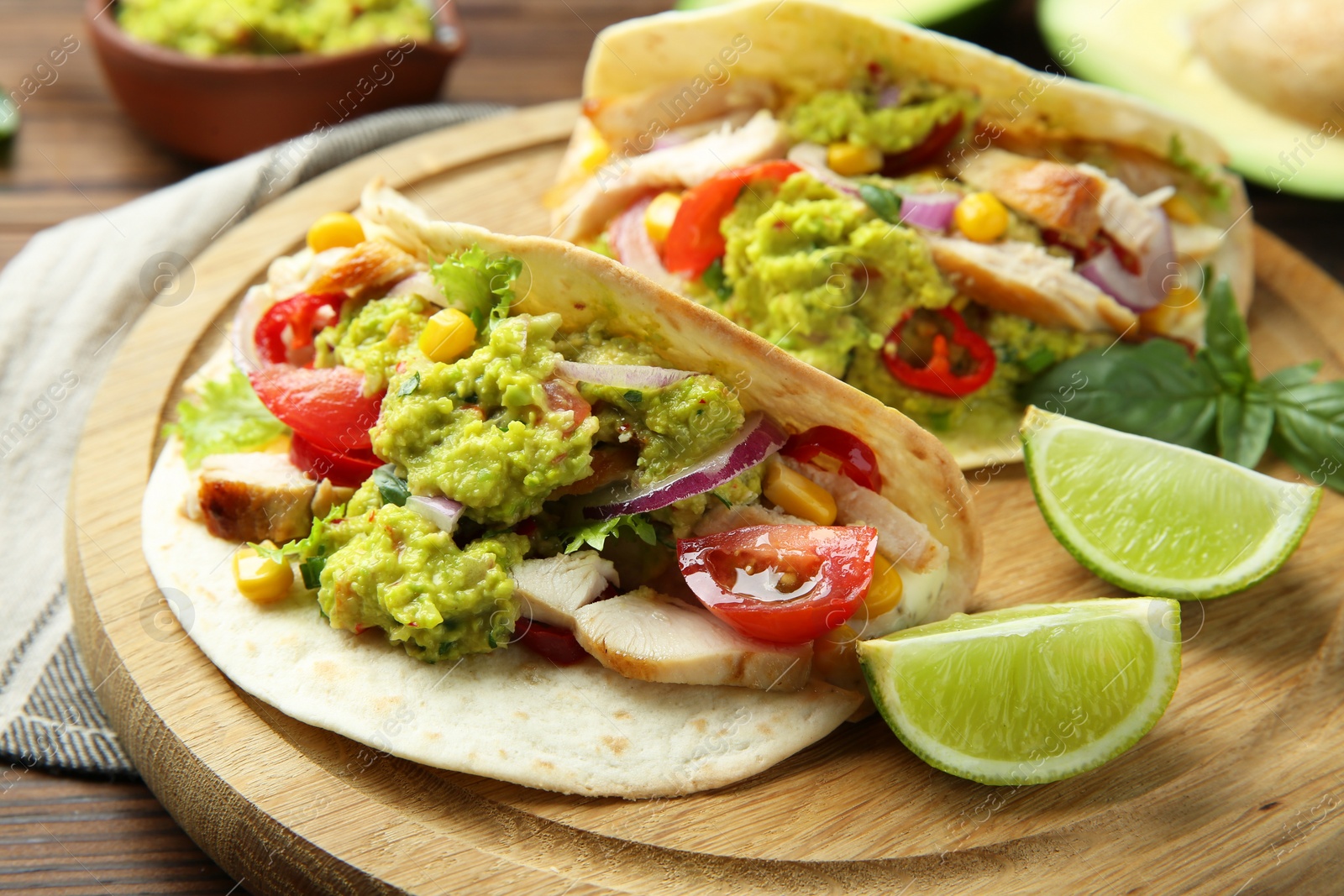 Photo of Delicious tacos with guacamole, meat and vegetables served with lime on wooden table, closeup