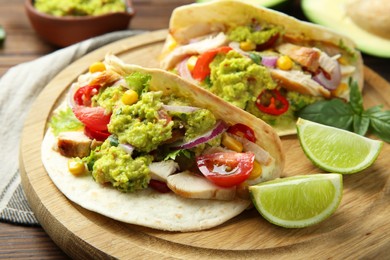 Delicious tacos with guacamole, meat and vegetables served with lime on wooden table, closeup