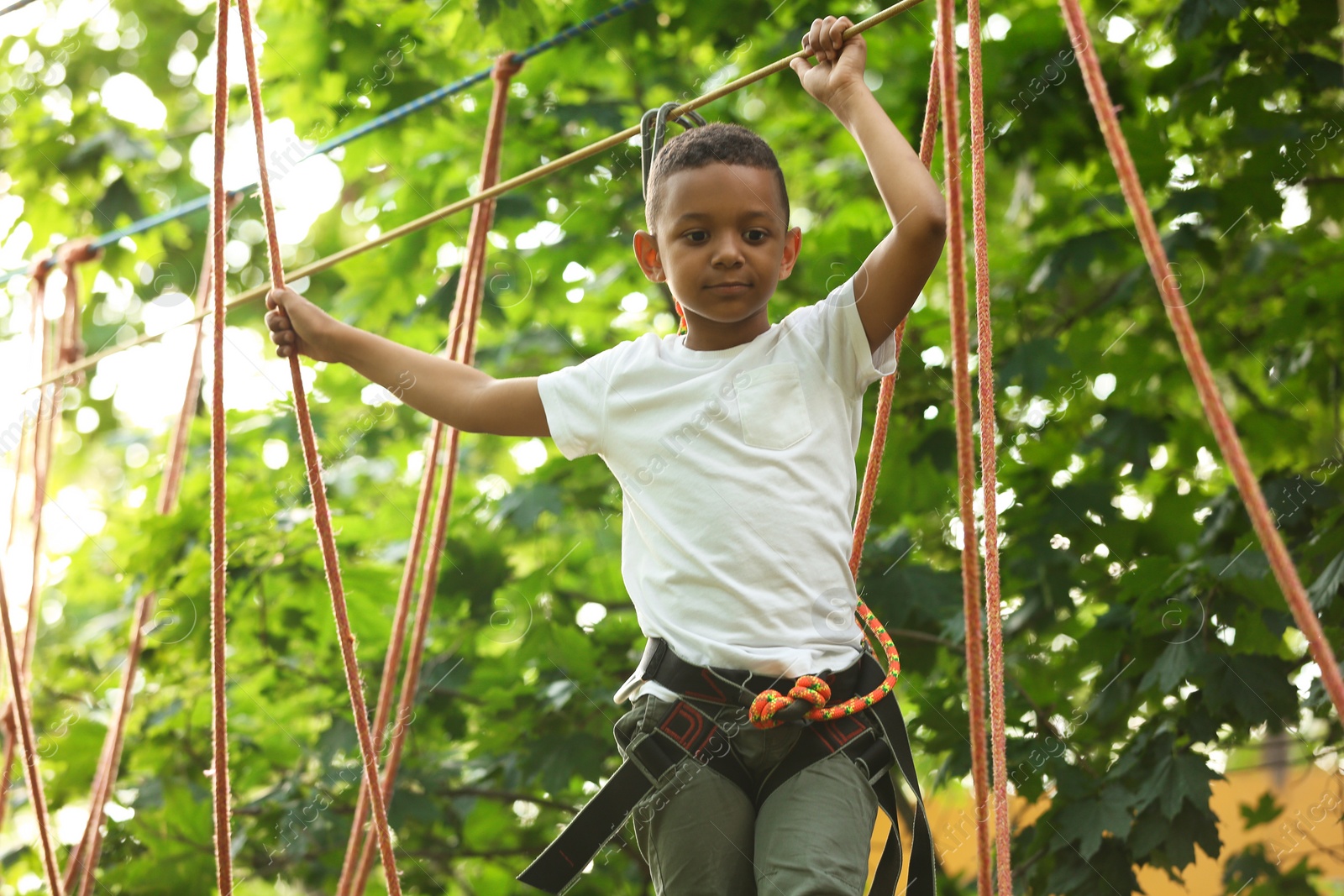 Photo of Little African-American boy climbing in adventure park. Summer camp