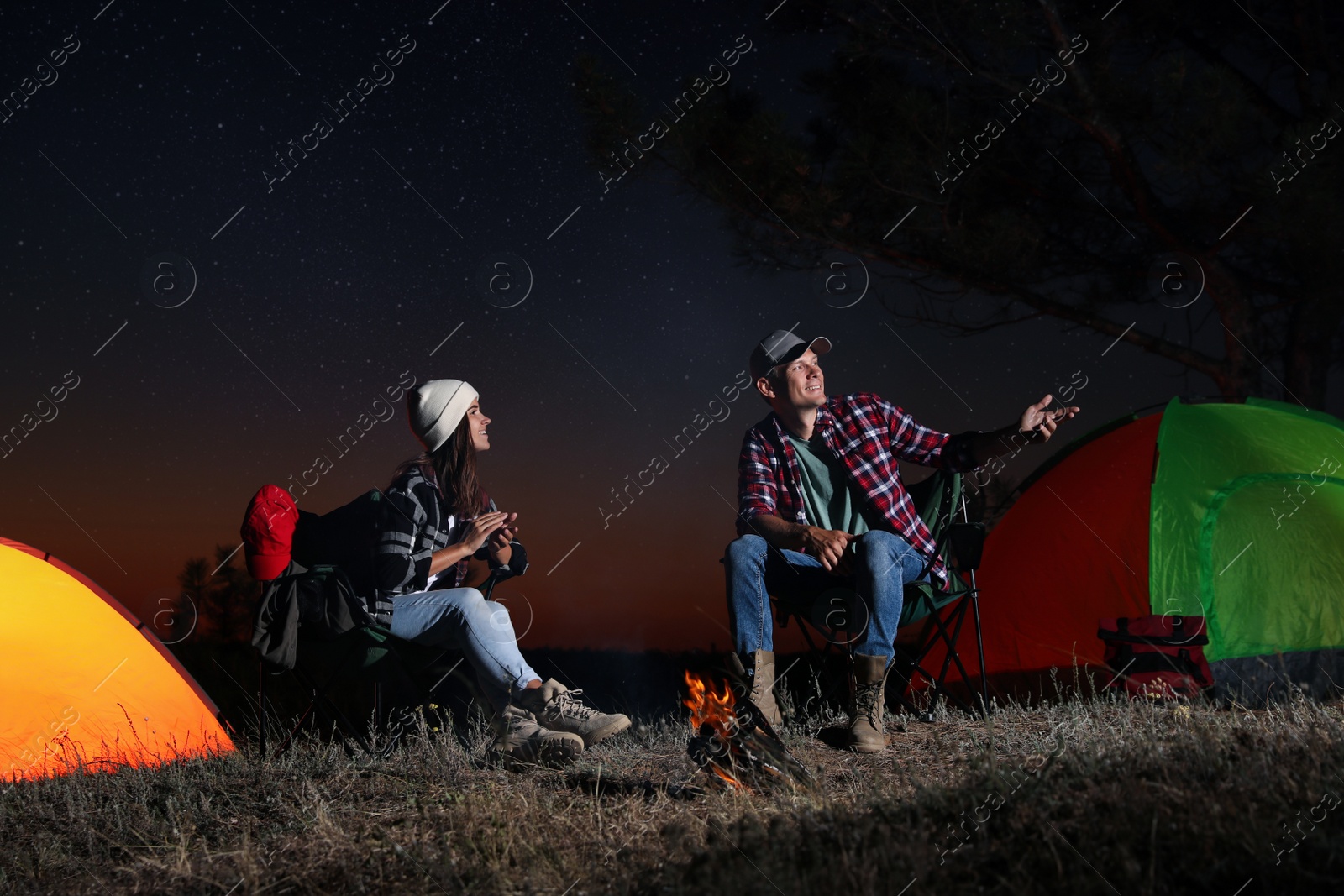 Photo of Couple near bonfire at night. Camping season