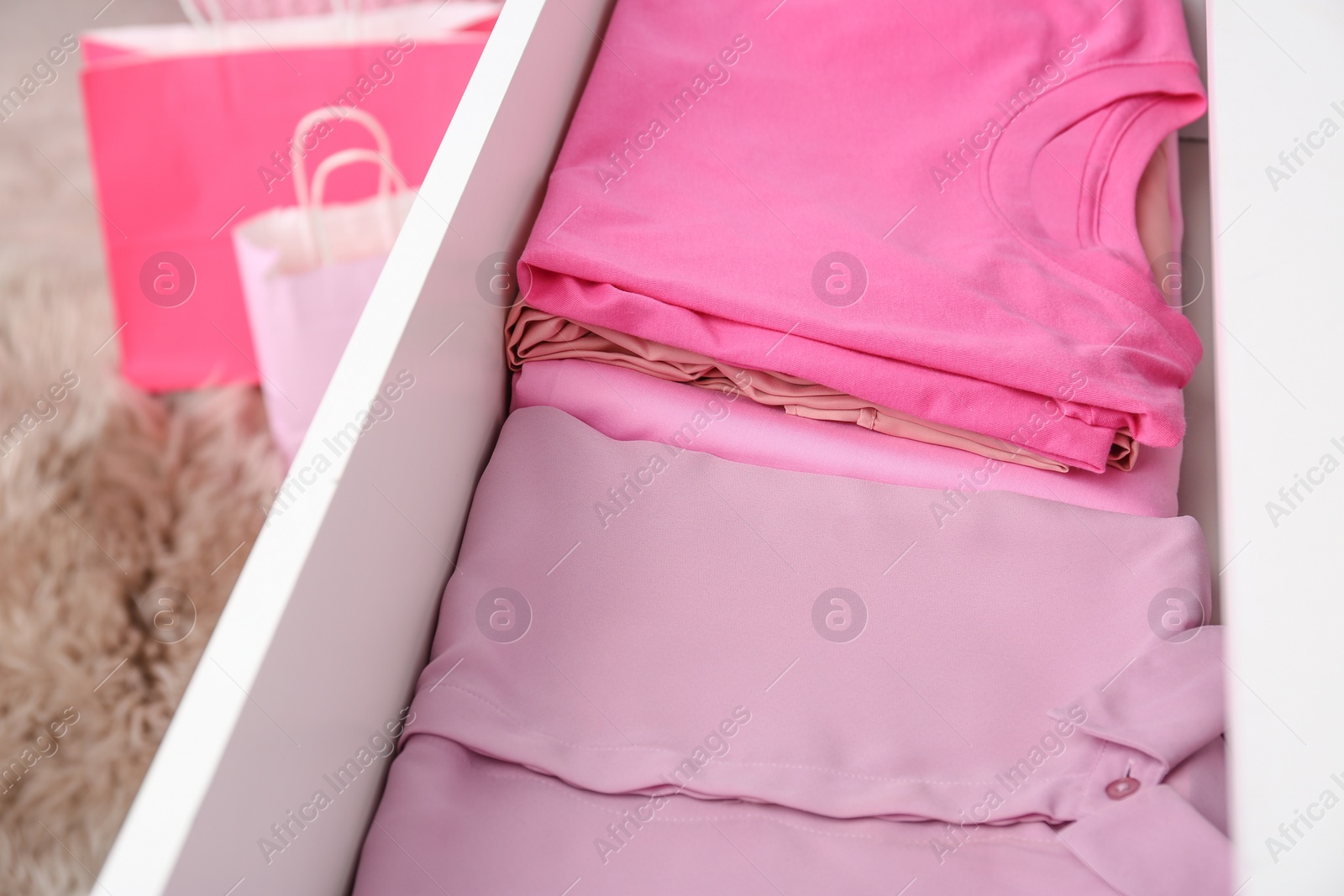 Photo of Many folded pink clothes in white chest of drawers indoors, closeup