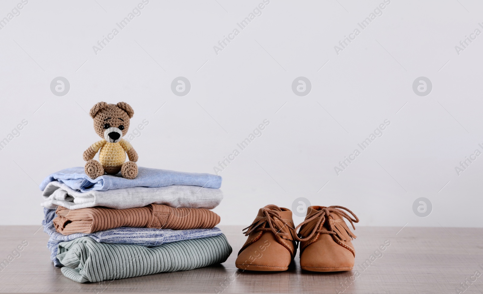Photo of Stack of baby boy's clothes, toy and shoes on wooden table against white background, space for text