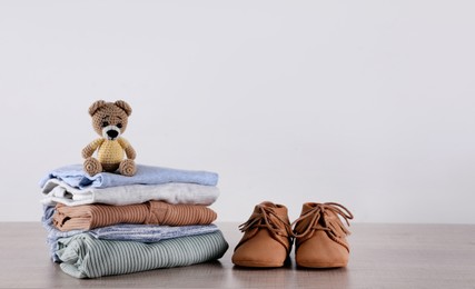 Stack of baby boy's clothes, toy and shoes on wooden table against white background, space for text