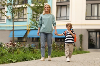 Photo of Happy woman and her little son on their way to kindergarten outdoors