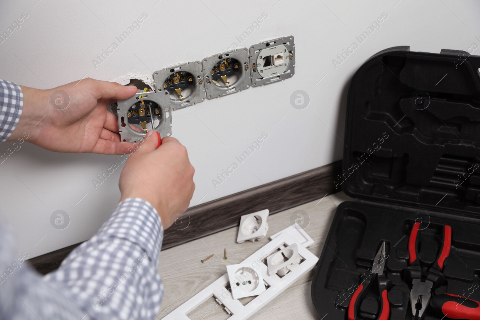 Photo of Electrician with screwdriver repairing power sockets indoors, closeup