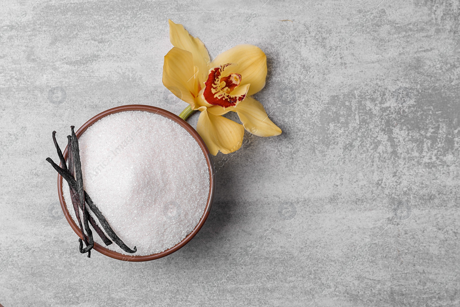 Photo of Bowl of aromatic vanilla sugar with flower and sticks on grey background