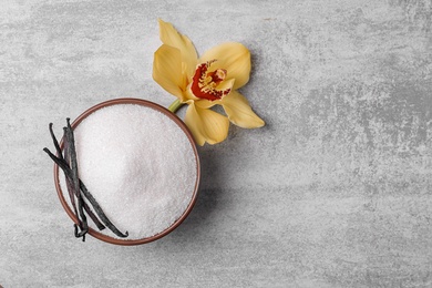 Photo of Bowl of aromatic vanilla sugar with flower and sticks on grey background