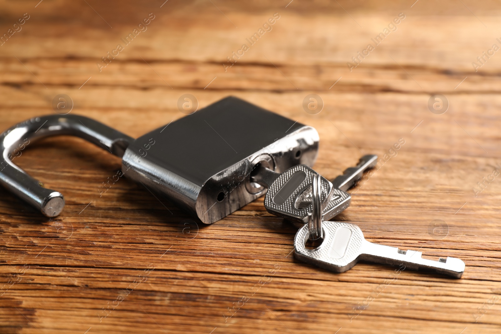Photo of Modern padlock with keys on wooden table, closeup