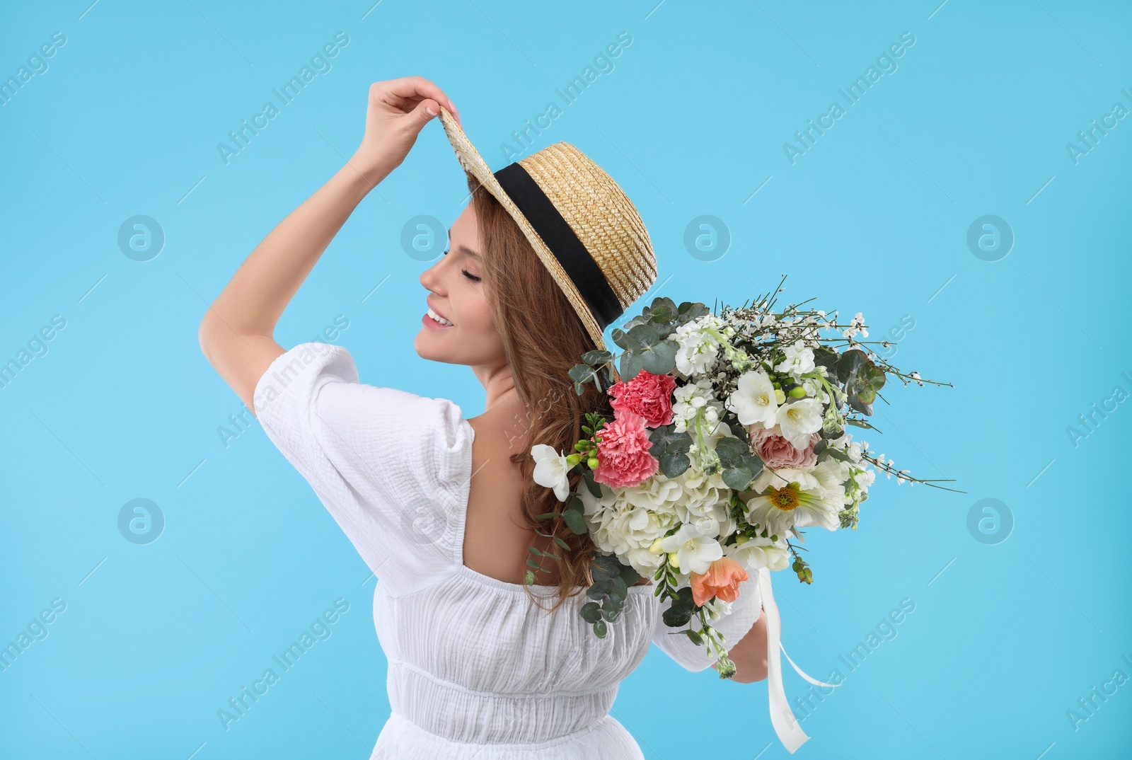 Photo of Beautiful woman in straw hat with bouquet of flowers on light blue background