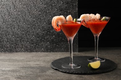 Photo of Tasty shrimp cocktail with sauce in glasses and lime on grey textured table, space for text