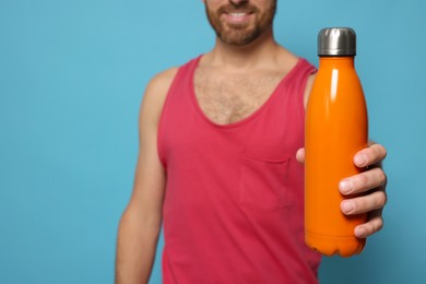 Man with orange thermo bottle against light blue background, closeup. Space for text