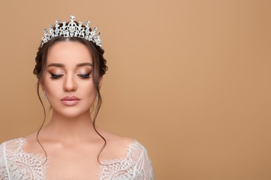 Beautiful young woman wearing luxurious tiara on beige background, space for text