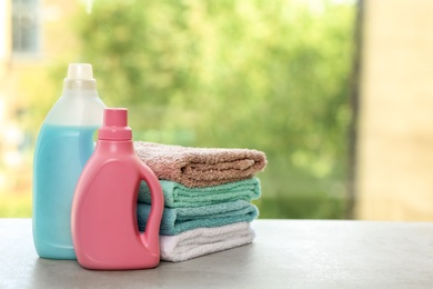 Stack of clean towels with detergents on table against blurred background. Space for text