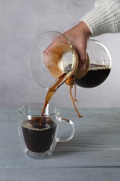 Woman pouring tasty drip coffee into cup at grey wooden table, closeup
