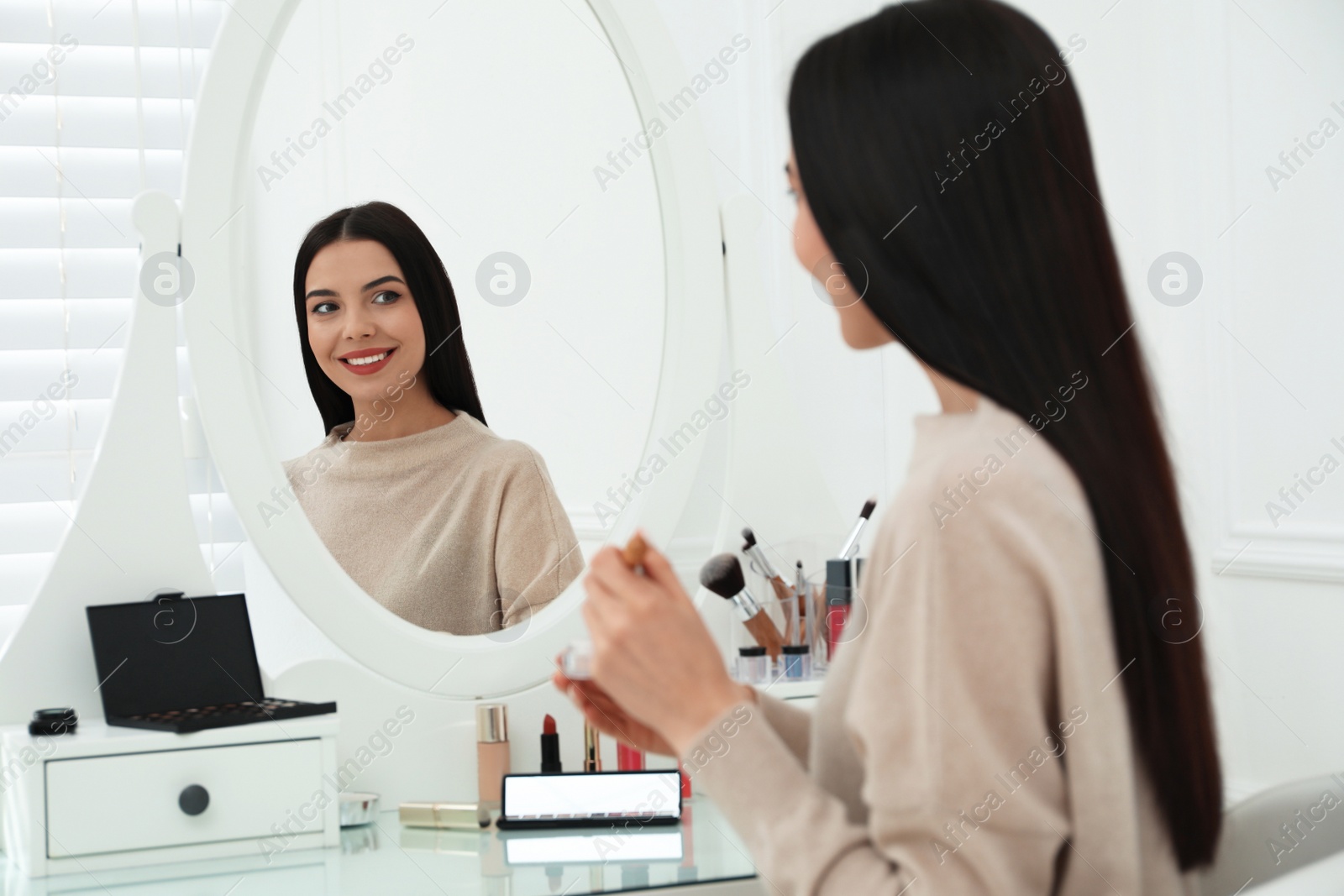 Photo of Beautiful woman applying makeup near mirror in room