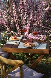 Photo of Delicious Belgian waffles with fresh strawberries and wine served on table in spring garden