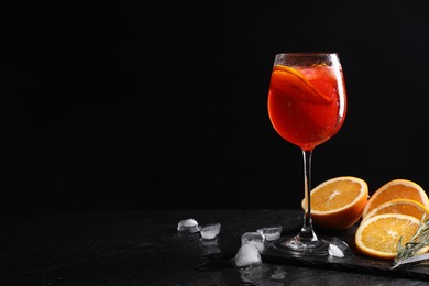 Photo of Glass of tasty Aperol spritz cocktail with orange slices and ice cubes on table against black background, space for text