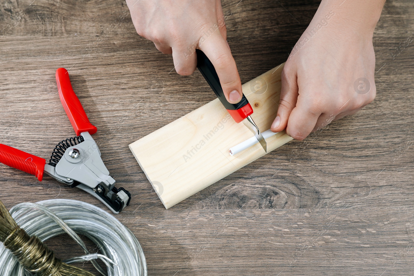 Photo of Professional electrician stripping wiring at wooden table, top view