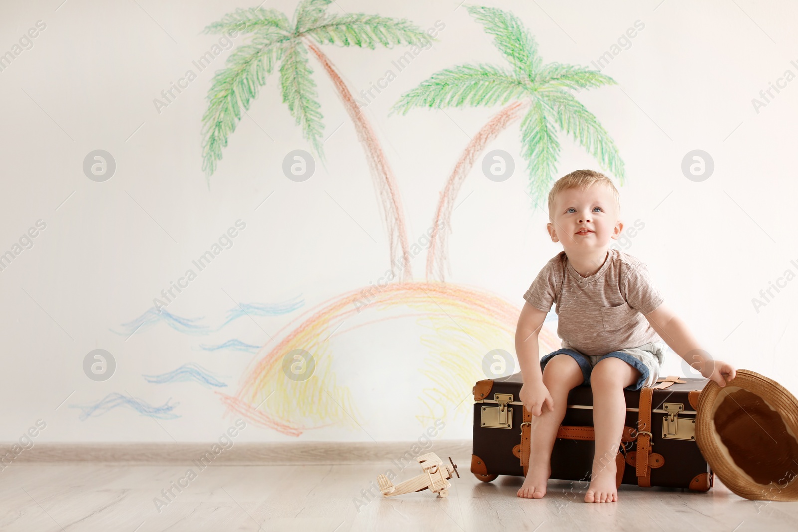 Photo of Adorable little child playing traveler with suitcase indoors