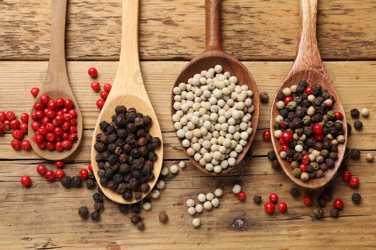 Photo of Aromatic spice. Different peppers in spoons on wooden table, flat lay