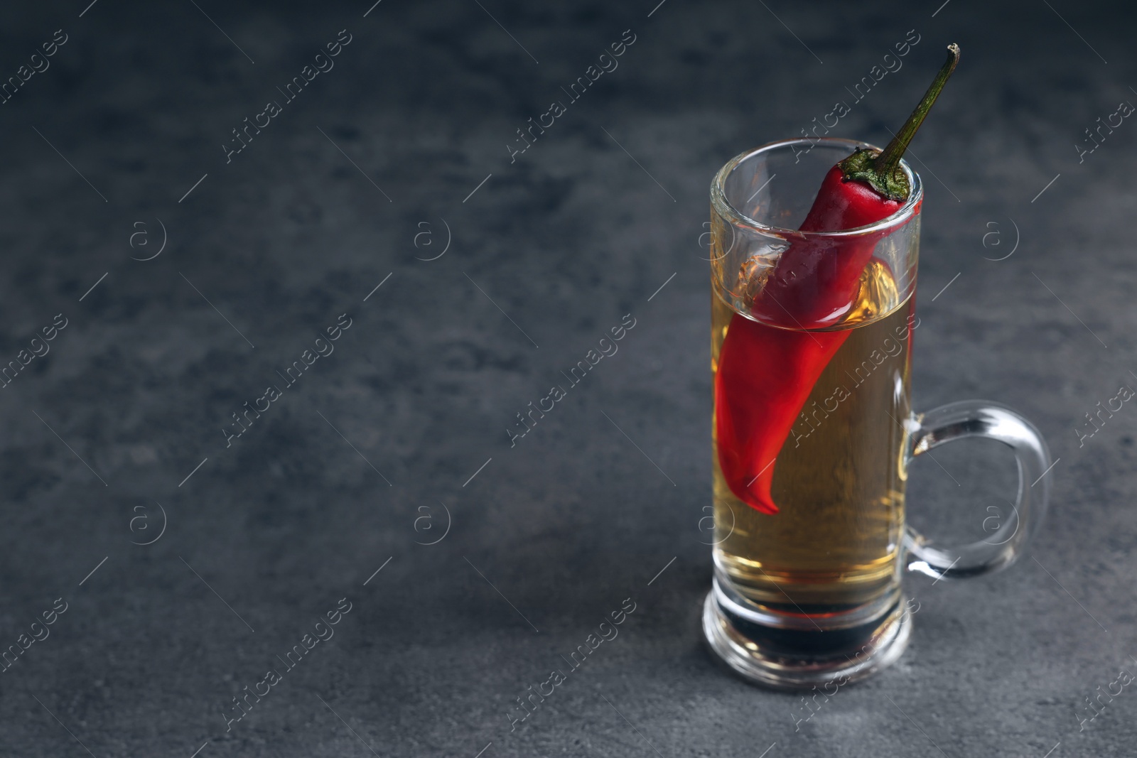 Photo of Red hot chili peppers and vodka in shot glass on grey table, space for text