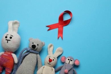 Photo of Cute knitted toys and red ribbon on blue background, flat lay. AIDS disease awareness