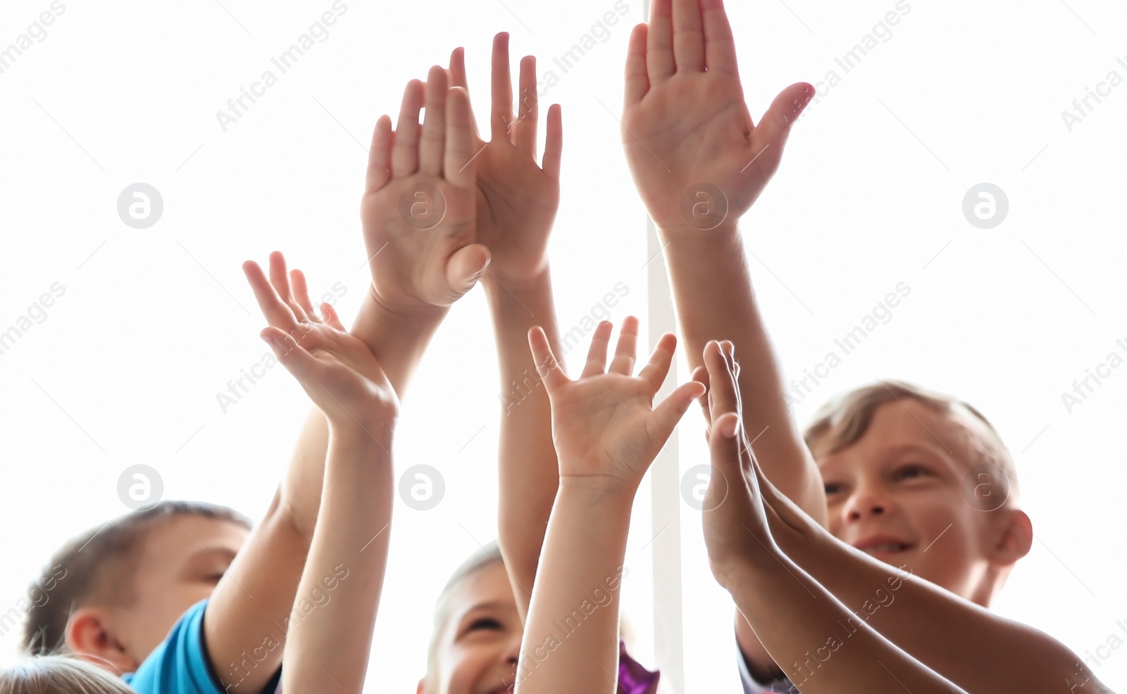 Photo of Little children raising hands together on light background. Unity concept