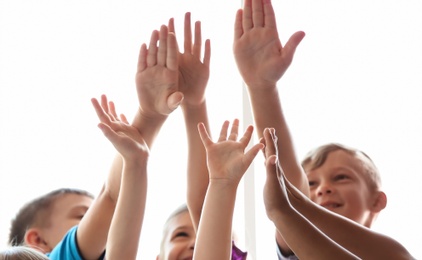 Photo of Little children raising hands together on light background. Unity concept