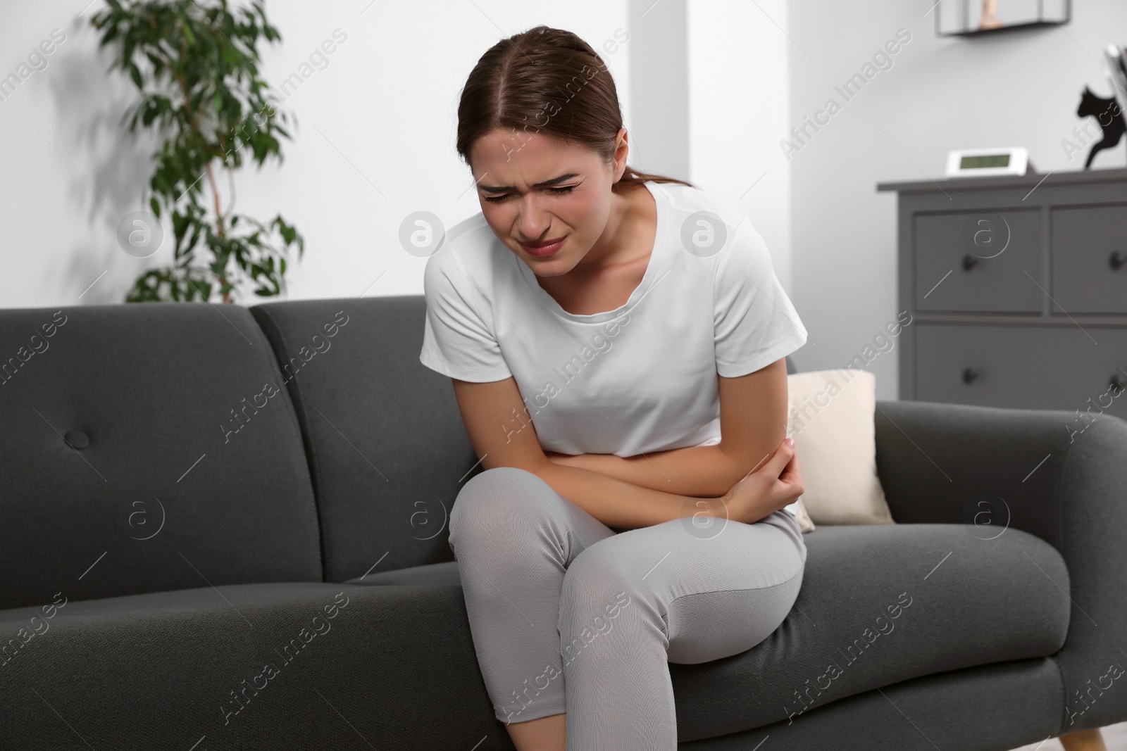 Photo of Young woman suffering from cystitis on sofa at home